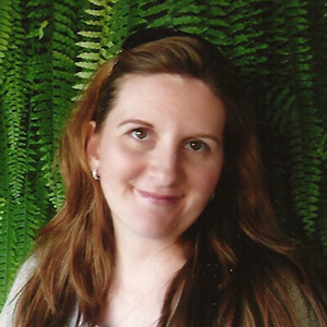 A woman smiling in front of a leafy backdrop